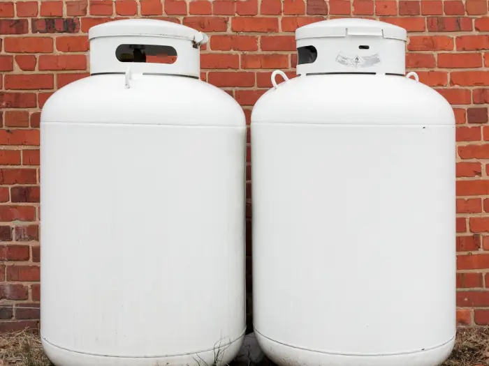 Two propane white canisters against brick wall.